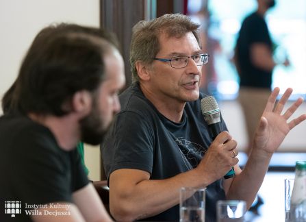 fotografia. spotkanie literacki środek europy w ramach festiwalu art piknik w willi decjusza. zaproszeni goście dyskutują przy długim stole w sali marceliny czartoryskiej. aleksander kaczorowski mówi do mikrofonu.